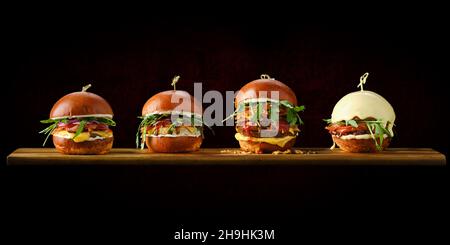 Ensemble de quatre hamburgers avec différents types de viande sur une table de service en bois Banque D'Images