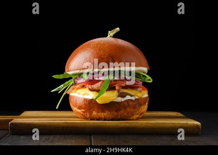 Hamburger avec bœuf et bacon croustillant sur plateau de service en bois sur fond noir Banque D'Images