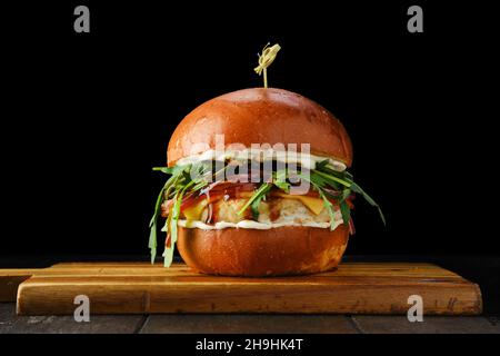 Hamburger avec patty de poulet sauce teriyaki sur plateau de service en bois sur fond noir Banque D'Images