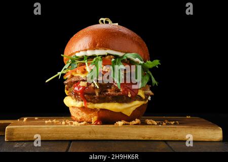 Hamburger avec deux côtelettes de bœuf et bacon sur une table de service en bois sur fond noir Banque D'Images