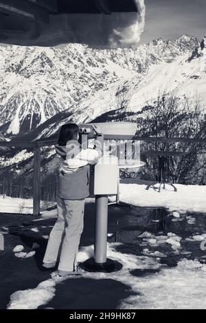Skieur fille regarde à travers des jumelles sur pont d'observation de la station de ski en hiver à la montagne journée ensoleillée. Montagnes du Caucase. Région de Svaneti, Hatsvali Banque D'Images