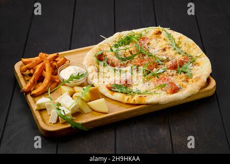 Focaccia à la tomate et au parmesan servi avec du fromage et des patates douces frites sur un plateau en bois Banque D'Images