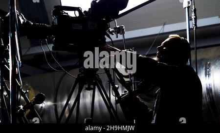 Un caméraman professionnel prend des concerts.Films.L'homme dans la nuit derrière les scènes met en place un appareil photo professionnel pour filmer un concert. Banque D'Images