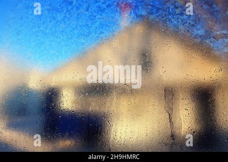 Vue de la maison sur la rue de l'intérieur à travers le verre de fenêtre embué avec des gouttes d'eau.Arrière-plan abstrait.Image floue.Effet de flou artistique. Banque D'Images