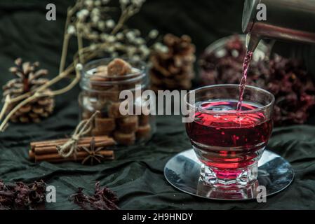 Le thé de Roselle (sorrel jamaïcain, Rozelle ou hibiscus sabdariffa) est versé d'une bouilloire dans une tasse en verre avec le roselle sec et le cube de sucre de canne brun. Guérir Banque D'Images