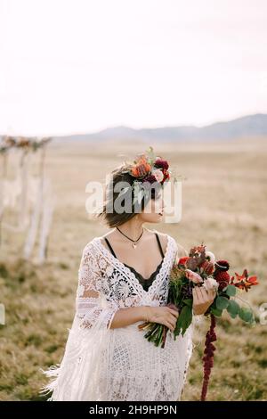 Mariée dans une couronne avec un bouquet de fleurs se tient dans un champ Banque D'Images