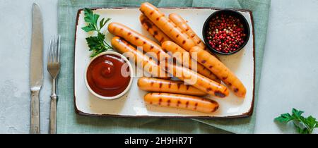 Saucisses grillées au barbecue avec sauce et ketchup et ail sur plaque de céramique sur fond de béton foncé.Vue de dessus. Banque D'Images