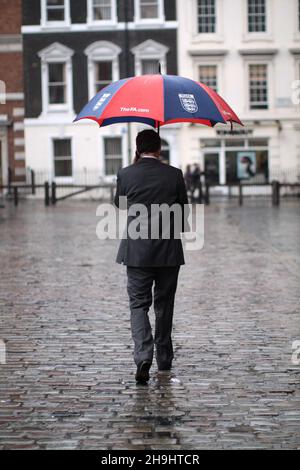 Un homme se protège de la pluie sous un parapluie FA à Covent Garden, Londres Banque D'Images