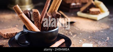 Morceaux de chocolat poreux et de bâtons de cannelle dans une tasse de café noir sur fond ancien sombre.Mise au point sélective. Banque D'Images