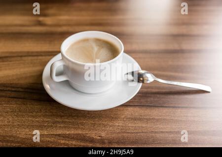 Une tasse de café chaud sur une soucoupe avec une cuillère se tient sur un fond en bois d'une table dans un café. Banque D'Images