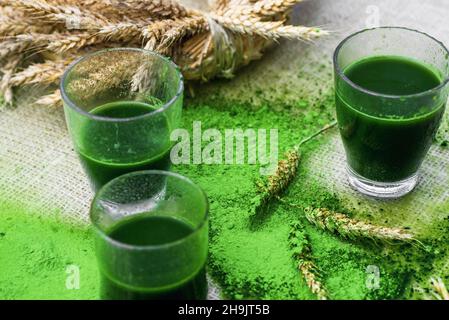 Trois verres avec des boissons de jeune orge verte et couronne de maïs sur fond arrosé de poudre d'orge verte. Banque D'Images