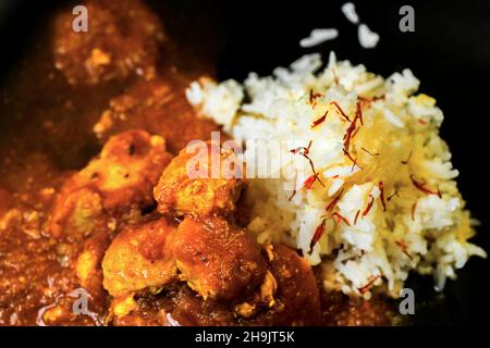 Détail des morceaux de curry de poulet à la sauce épicée (style madras) et riz basmati au safran sur fond noir, gros plan.Cuisine indienne traditionnelle Banque D'Images