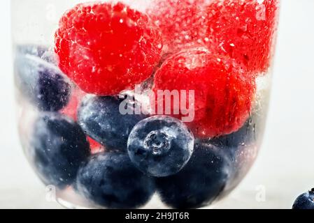 Myrtille et framboise en verre avec boisson froide à l'eau de soude, photographiée à travers le verre dépoli, gros plan. Banque D'Images