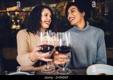 Couple multiracial de jeunes meilleurs amis célébrant la dégustation avec du vin rouge - des amies multiculturelles qui se tringuent au restaurant avec des lunettes de vin Banque D'Images