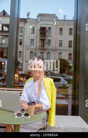 Jeune femme joyeuse utilisant un ordinateur portable dans un café extérieur Banque D'Images