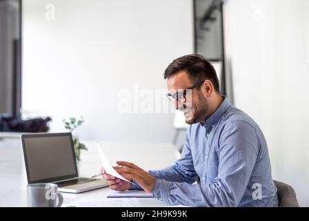 Jeune souriant gai homme d'affaires confiant et confiant entrepreneur vérifiant le plan de travail horaire ou horaire business deal document accord dans la copie de bureau Banque D'Images