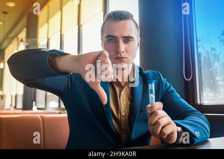La main d'un homme d'affaires sérieux montre un mauvais geste d'un doigt vers le bas à côté d'un sablier temps. Banque D'Images