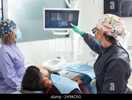 Inspection à l'aide d'une macro-caméra dentaire et affichage du résultat sur le moniteur.Jeune femme dentiste traitant les canaux racinaires dans la clinique dentaire.Homme patie Banque D'Images