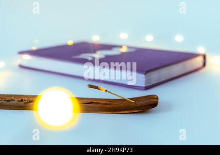 Gros plan bâton d'encens brûlant avec un journal de lune avec fond de lumières de Noël.Concept : pratiques spirituelles d'autosoins Banque D'Images