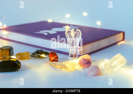 Gros plan de cristal d'ange de quartz clair près d'un journal de lune avec des lumières de Noël et de l'encens sur fond.Concept : pratiques spirituelles d'autosoins Banque D'Images