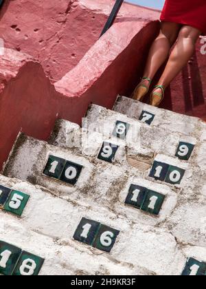 Les pattes brunes d'une femme en robe rouge, au bout d'une des marches en pierre avec des chiffres, sur la Plaza de Toros de Mijas, Málaga. Banque D'Images