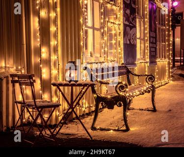 Hafnarfjordur, Islande - 4 décembre 2021 : banc et table avec une lanterne aux chandelles devant le restaurant A. Hansen, recouvert de neige.Nuit d'hiver. Banque D'Images