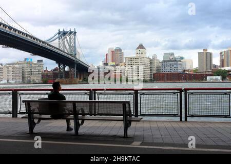 Une personne assise sur un banc qui regarde la rivière East et le quartier DUMBO à Brooklyn, New York.28 août 2011 Banque D'Images