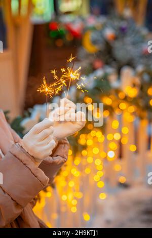 Gros plan des mains des femmes dans des moufles blanches tenant le sparkler brûlant.Fête du nouvel an, lumière de Noël.Concept de vacances Banque D'Images