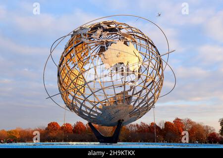 L'Australie et l'Océanie se glose orange sur le Unisphere pendant un coucher de soleil d'automne tandis qu'un avion survole le parc Flushing Meadows-Corona, New York, NY. Banque D'Images