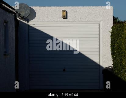 Porte de garage blanche avec la moitié à l'ombre et la moitié à la lumière du soleil. Banque D'Images