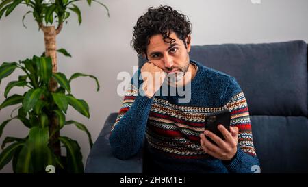 Dépression masculine tenant son front tout en ayant des maux de tête sur le canapé à la maison.Homme adulte utilisant le smartphone et la pensée, ayant de lourdes pensées, le breake vers le haut Banque D'Images