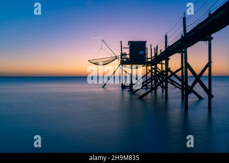 Vieux cabanes de pêche en bois typiques sur pilotis appelées « carrelet » dans l'océan atlantique près de la Rochelle, France. Photo prise au coucher du soleil. Banque D'Images