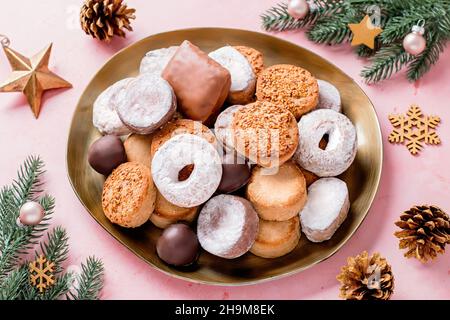 Les délices des fêtes polvorones et les mantecados en assiette dorée sur table rose décorée de boules dorées, branches d'arbre de noël et cônes de pin, haut Banque D'Images