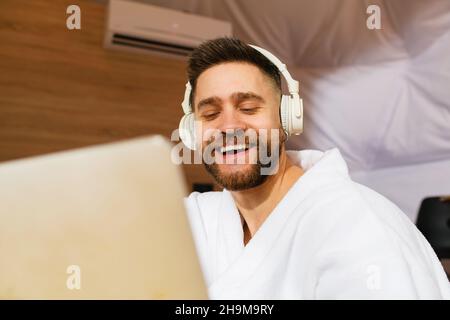 Jeune beau barbu avec casque et ordinateur portable.Gros plan.L'homme ferme les yeux et sourit. Banque D'Images