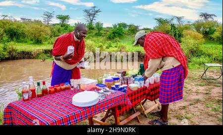 Masai Mara, Kenya - 26 septembre 2013. Deux guides safari Maasai portant des vêtements tribaux traditionnels préparent une collation matinale pour les clients. Banque D'Images