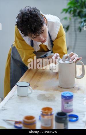 Une jeune femme en tablier apprend à fabriquer de la céramique pendant la masterclass en atelier de poterie Banque D'Images