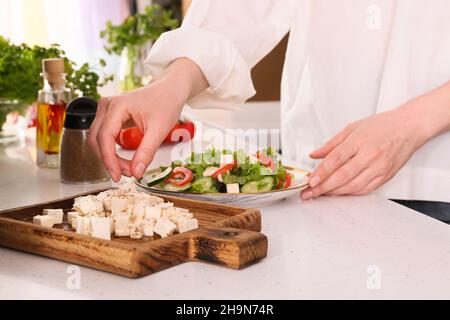 Femme faisant de la salade grecque avec du fromage feta coupé sur la table dans la cuisine Banque D'Images