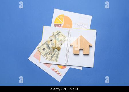 Carnet avec maison en bois, argent et diagrammes sur fond bleu Banque D'Images