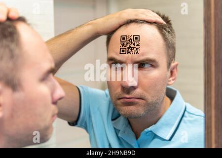 Un homme avec une expression stupide regarde son code qr sur sa tête. Le concept de chipping de la population. Jeune homme avec un code qr sur son front. glo Banque D'Images