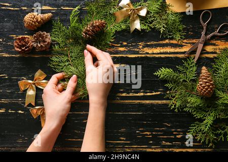 Femme décorant belle couronne de Noël faite de branches de sapin sur la table Banque D'Images