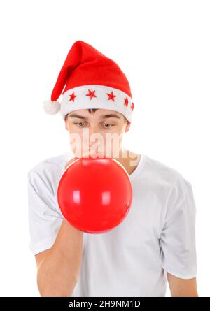 Adolescent dans le chapeau du Père Noël gonfler ballon rouge isolé sur le fond blanc Banque D'Images