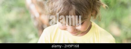 flou de mouvement photo défoqué de portrait sourire enfant ensoleillé candid caucasien garçon avec blond long ondulé ou cheveux bouclés et lumière du soleil sur le visage sur la nature pays Banque D'Images