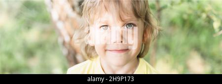 flou de mouvement photo défoqué de portrait sourire enfant ensoleillé candid caucasien garçon avec blond long ondulé ou cheveux bouclés et lumière du soleil sur le visage sur la nature pays Banque D'Images