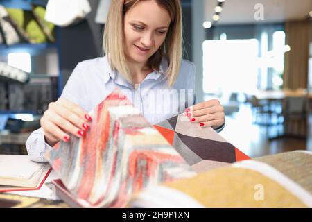 Une femme décoratrice choisit des tissus pour rideaux broder des tissus tapis dans une salle d'exposition textile Banque D'Images