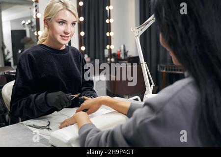 Joyeux maître attrayant faisant des soins de manucure avec l'équipement spécial dans le salon de manucure Banque D'Images