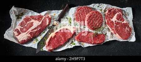 Vue de dessus de divers steaks de bœuf à la ribeye et à la sirloin non cuits préparés avec des côtelettes de hamburger et un couteau aiguisé assaisonné d'herbes Banque D'Images