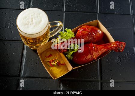 De dessus de l'appétissant pilons de poulet servis avec des feuilles de laitue et de la sauce placée près d'un verre de bière sur table noire dans le café Banque D'Images