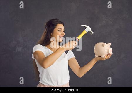 Une femme heureuse avec un marteau dans ses mains va briser la tirelire qu'elle tient dans ses mains. Banque D'Images