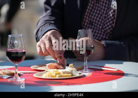 Homme mangeant des viandes de porc cuites et des verres de vin rouge sur une table lors d'un atelier "Apero sur un plateau, vins et fromages" (dégustation de vins et fromages) à Banque D'Images