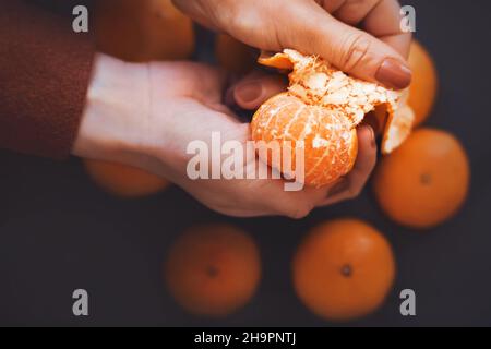 Une femme dans une veste de laine brune pelage une mandarine mûre délicieuse d'une peau d'orange.Des fruits sains.Agrumes pour Noël.Mois du nouvel an Banque D'Images